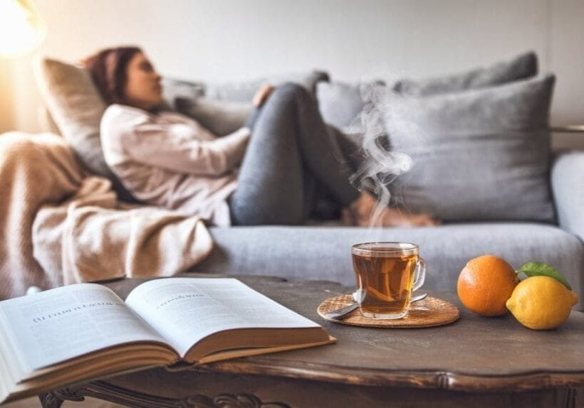 A scene of a cozy living room setting where someone is curled up on a modern couch with a soft blanket.