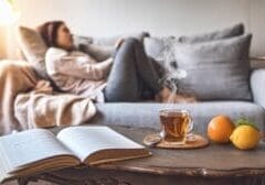 a-cozy-living-room-setting-with-a-modern_efVG91WLT_aT9X7tmpMqAw_6SO9eNM4SuOnL5pO1KiwqQ A scene of a cozy living room setting where someone is curled up on a modern couch with a soft blanket.